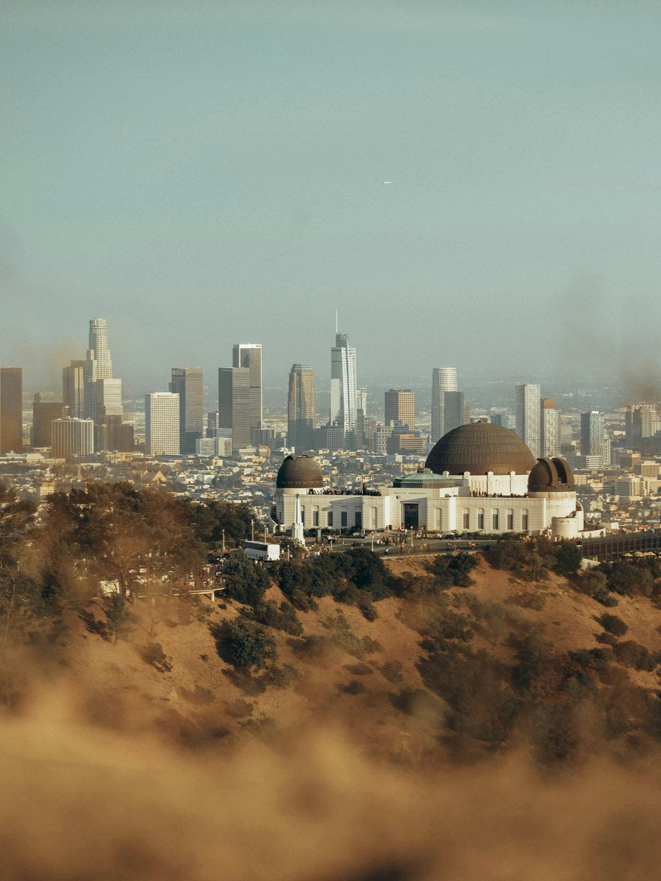 Griffith Observatory overlooks Los Angeles skyline on a hazy day; beige hills in the foreground.