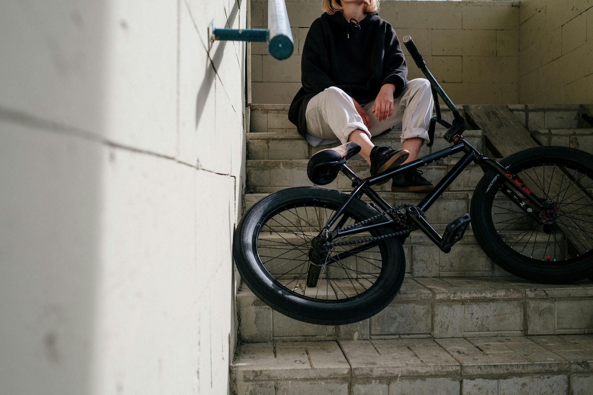 Person sitting on a black bicycle at the top of a concrete stairwell, holding a bottle.