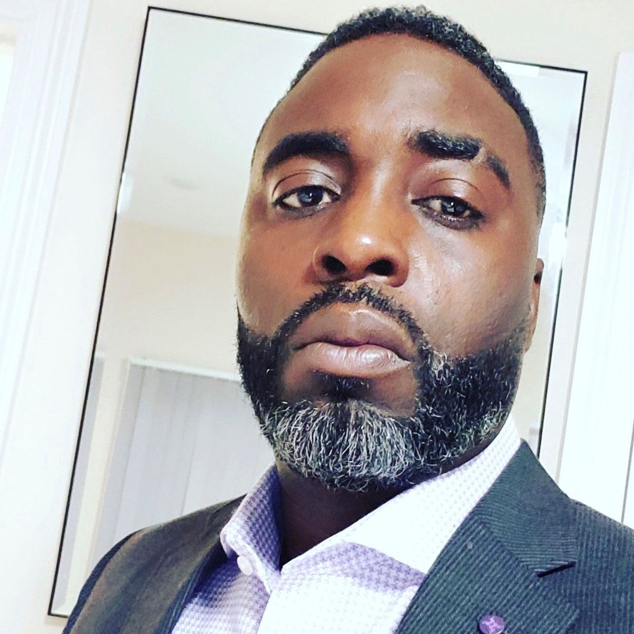 A man with a beard is wearing a suit and looking at the camera.