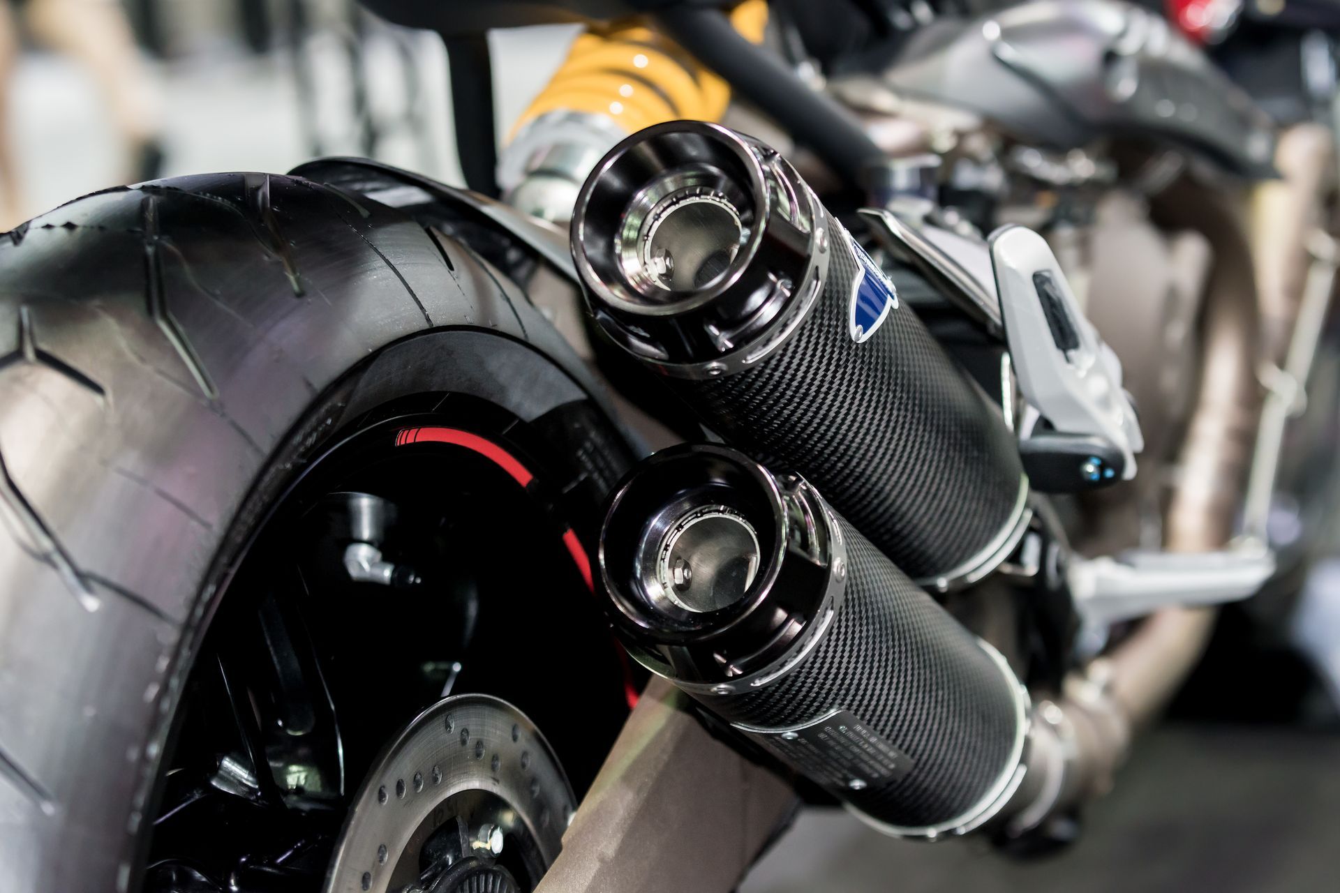 Close-up of a motorcycle’s twin carbon-fiber exhaust pipes and rear tire with red accents.
