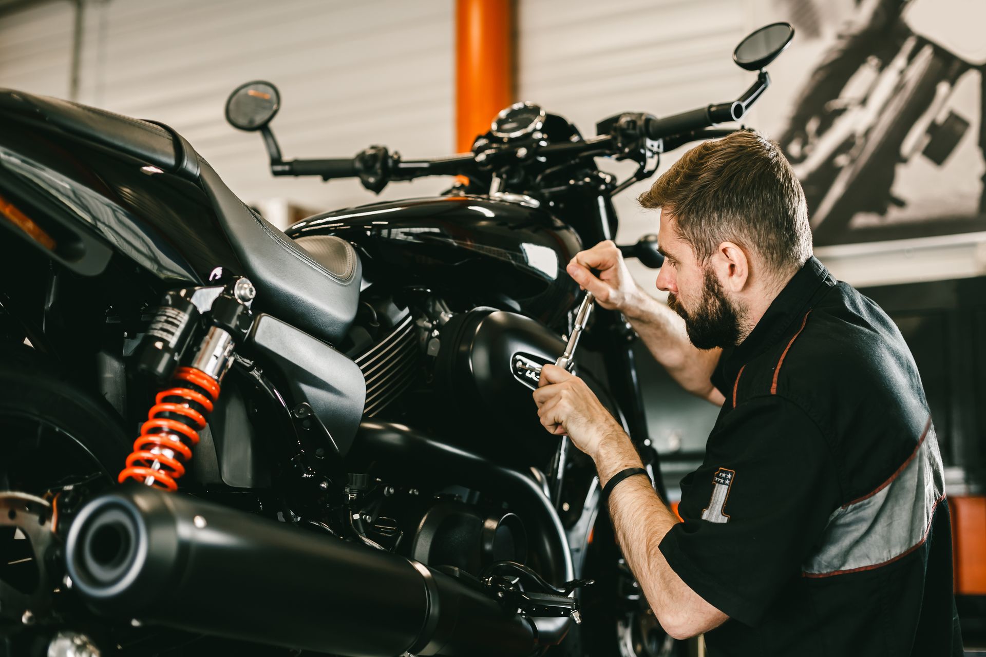 Mechanic repairing a black motorcycle in a garage, focused on the engine area.