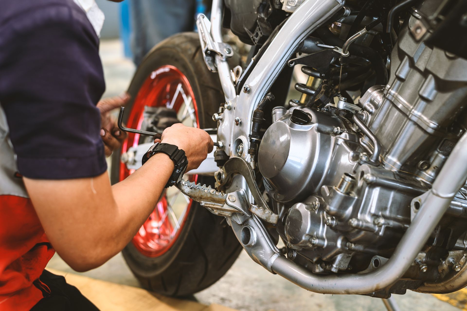 Mechanic adjusting a motorcycle engine beside a red rear wheel.