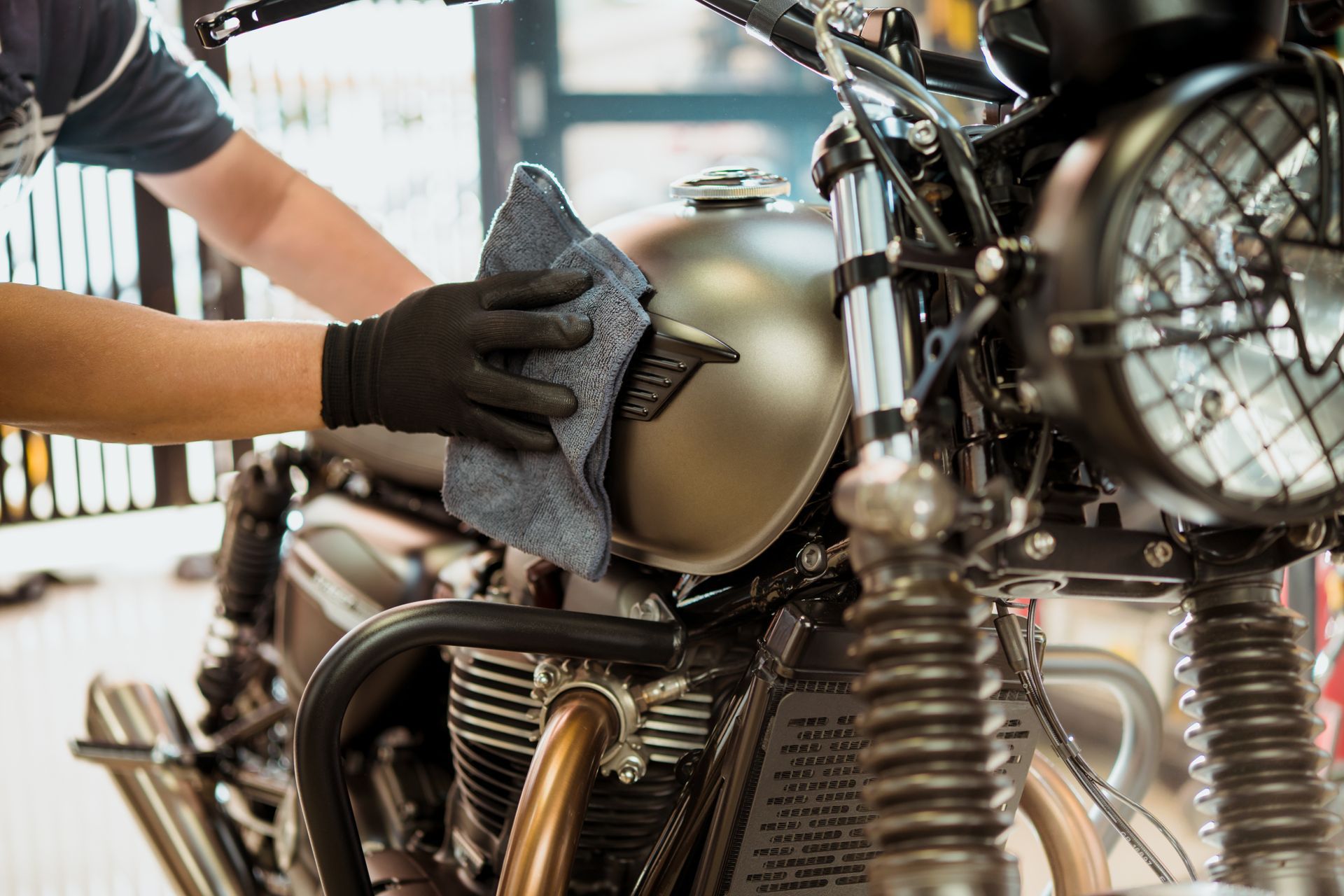 Person wiping a vintage motorcycle with a cloth in a garage.