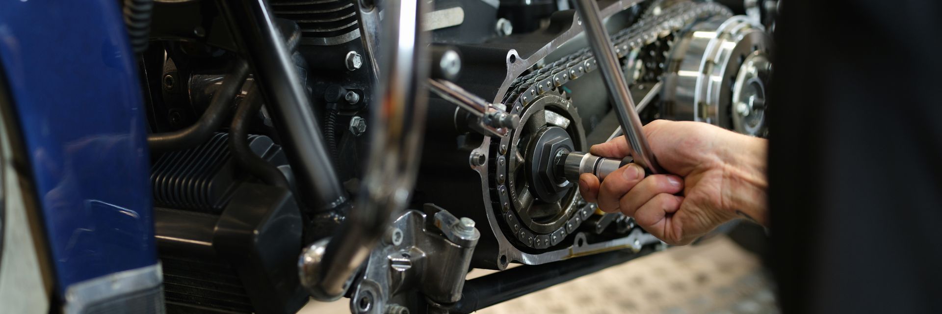 Close-up of a mechanic adjusting a motorcycle engine with tools in a workshop.