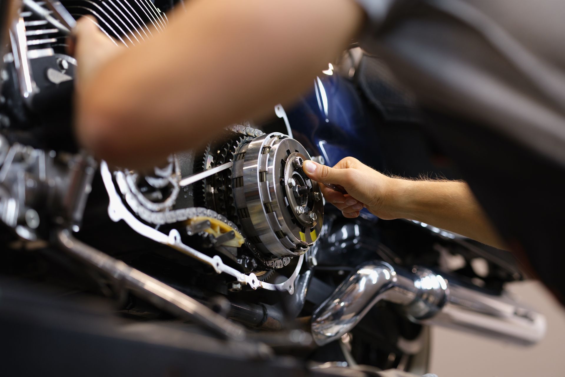 Hands working on a chrome motorcycle engine in a workshop.