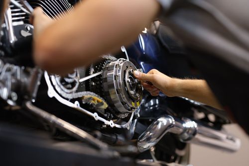 Hands working on a chrome motorcycle engine in a workshop.