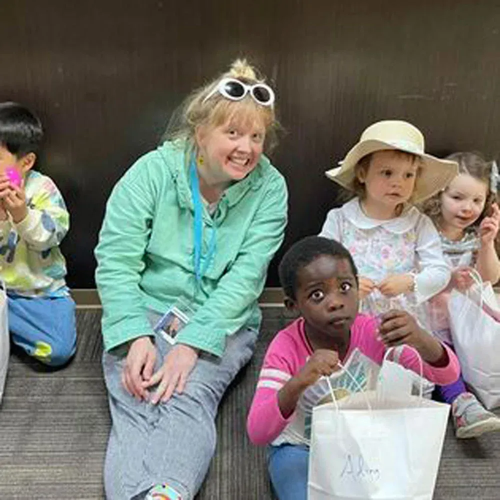 A woman and four children sit on a floor in front of a dark wall, interacting with gift bags.