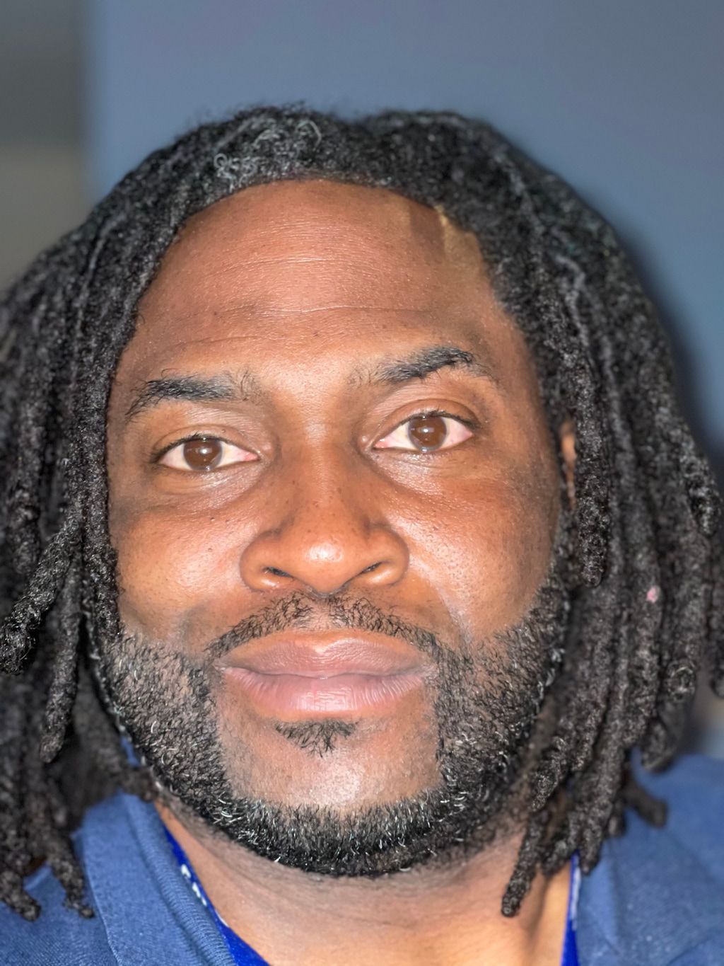 A man with dreadlocks and a beard is wearing a blue shirt.