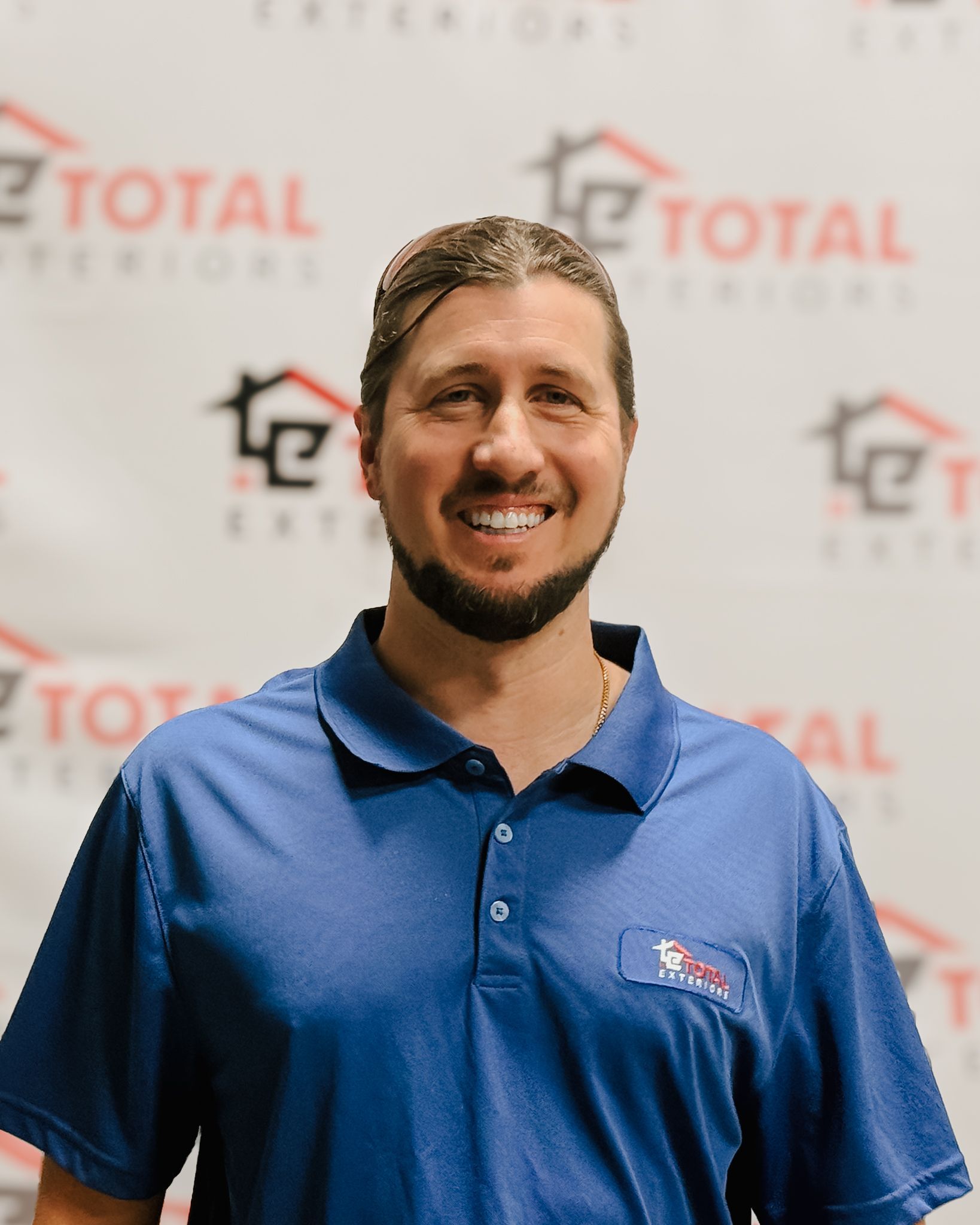 A man wearing glasses is standing in front of a wall that says total exteriors