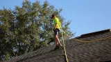 A man is standing on top of a roof holding a rope.