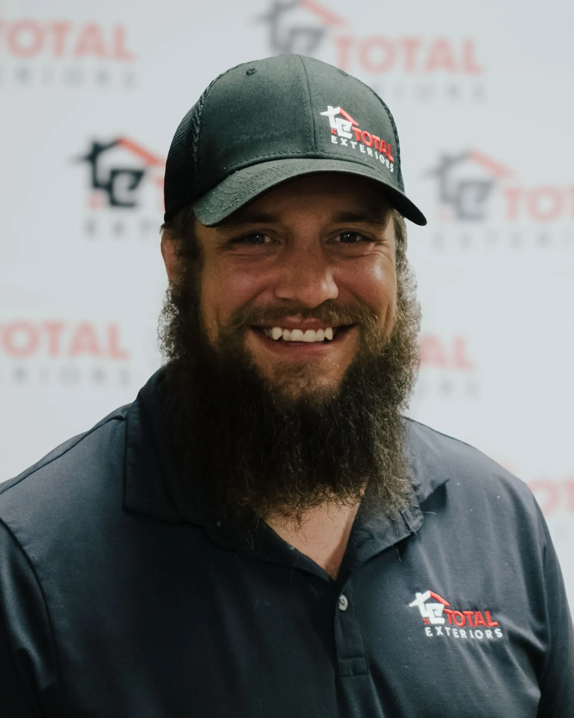 A man with a beard is wearing a hat and smiling.