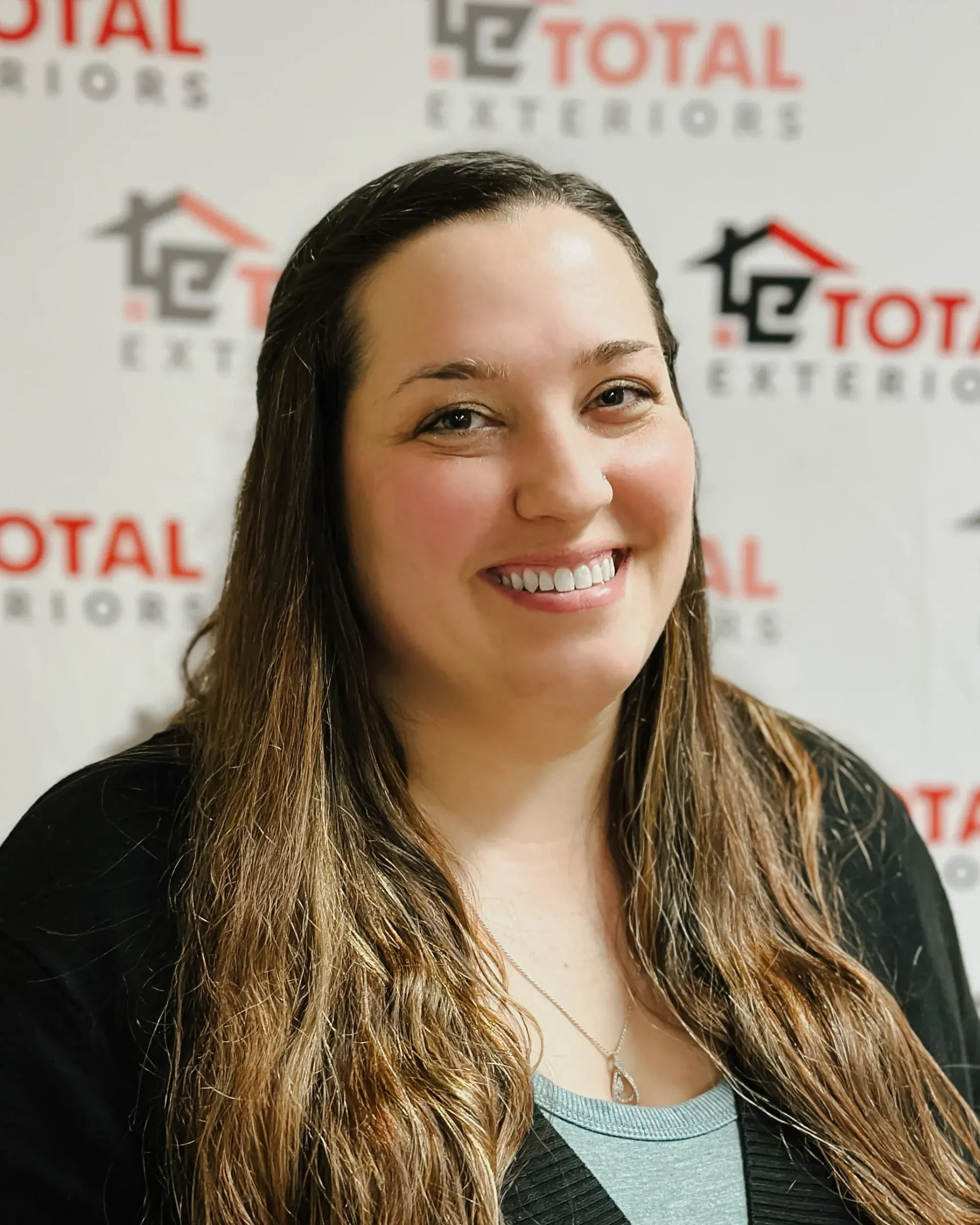 A woman is smiling in front of a total exteriors sign