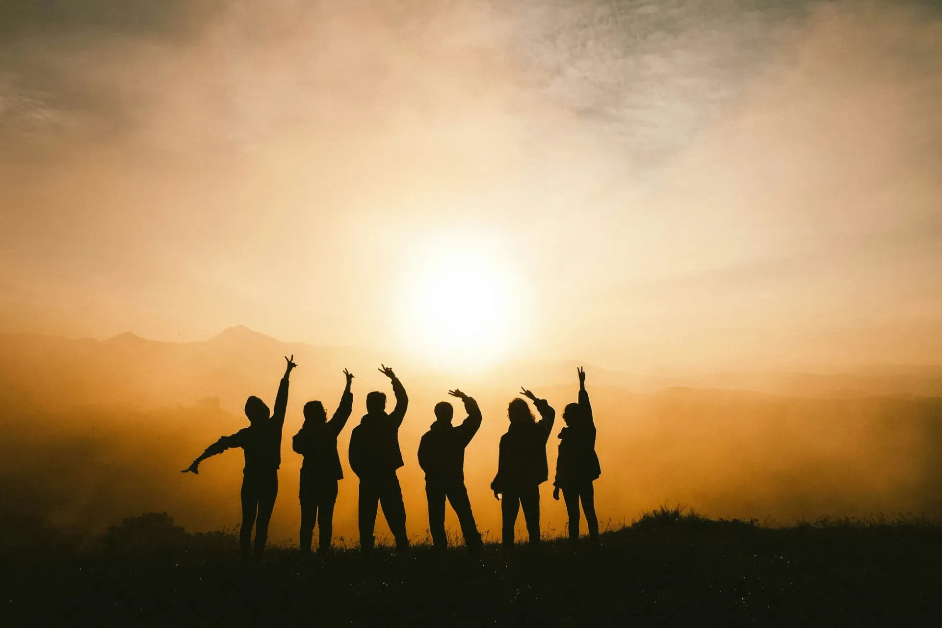 A group of people are standing on top of a hill at sunset.