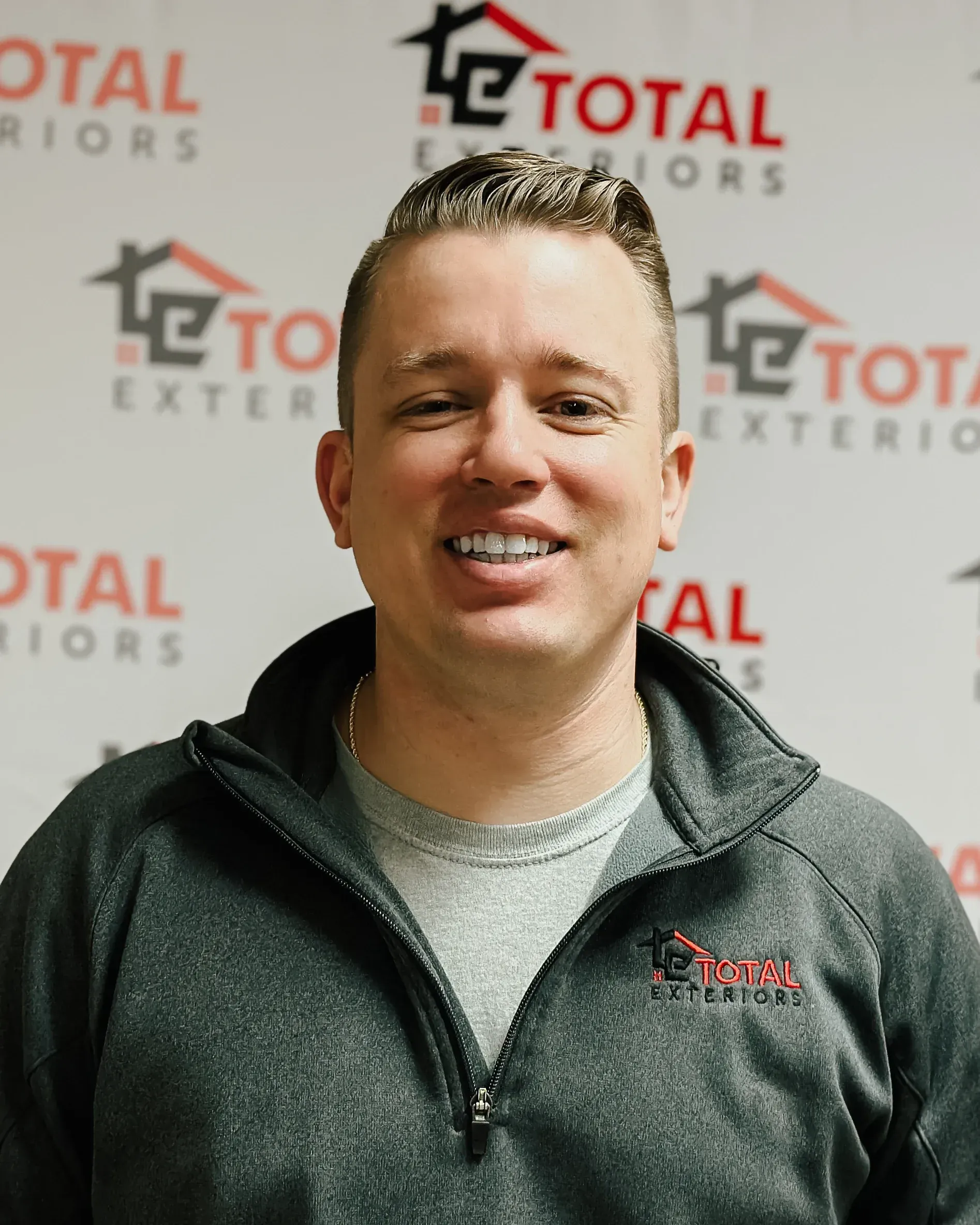 A man is smiling in front of a wall that says total exteriors