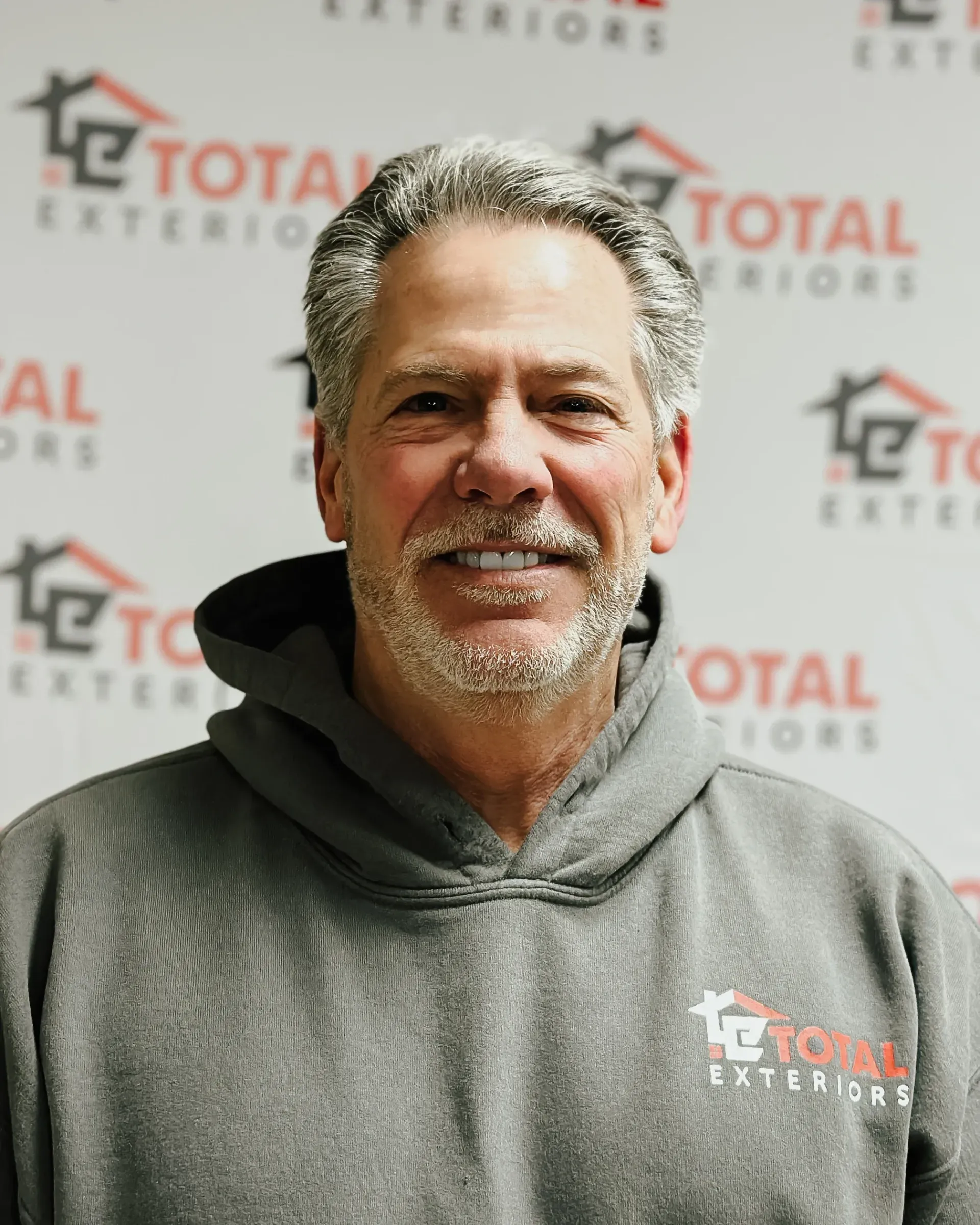A man wearing a total exteriors hoodie smiles for the camera