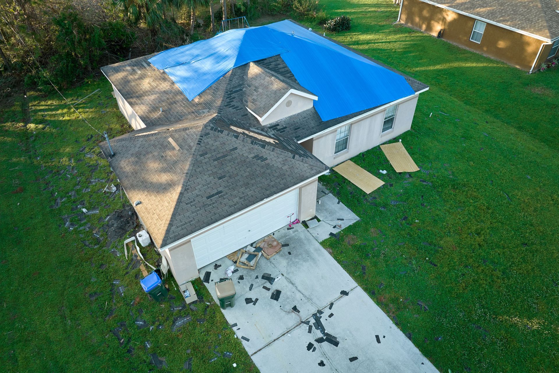Aerial view of a house with damaged roof and blue tarp. Debris on driveway.