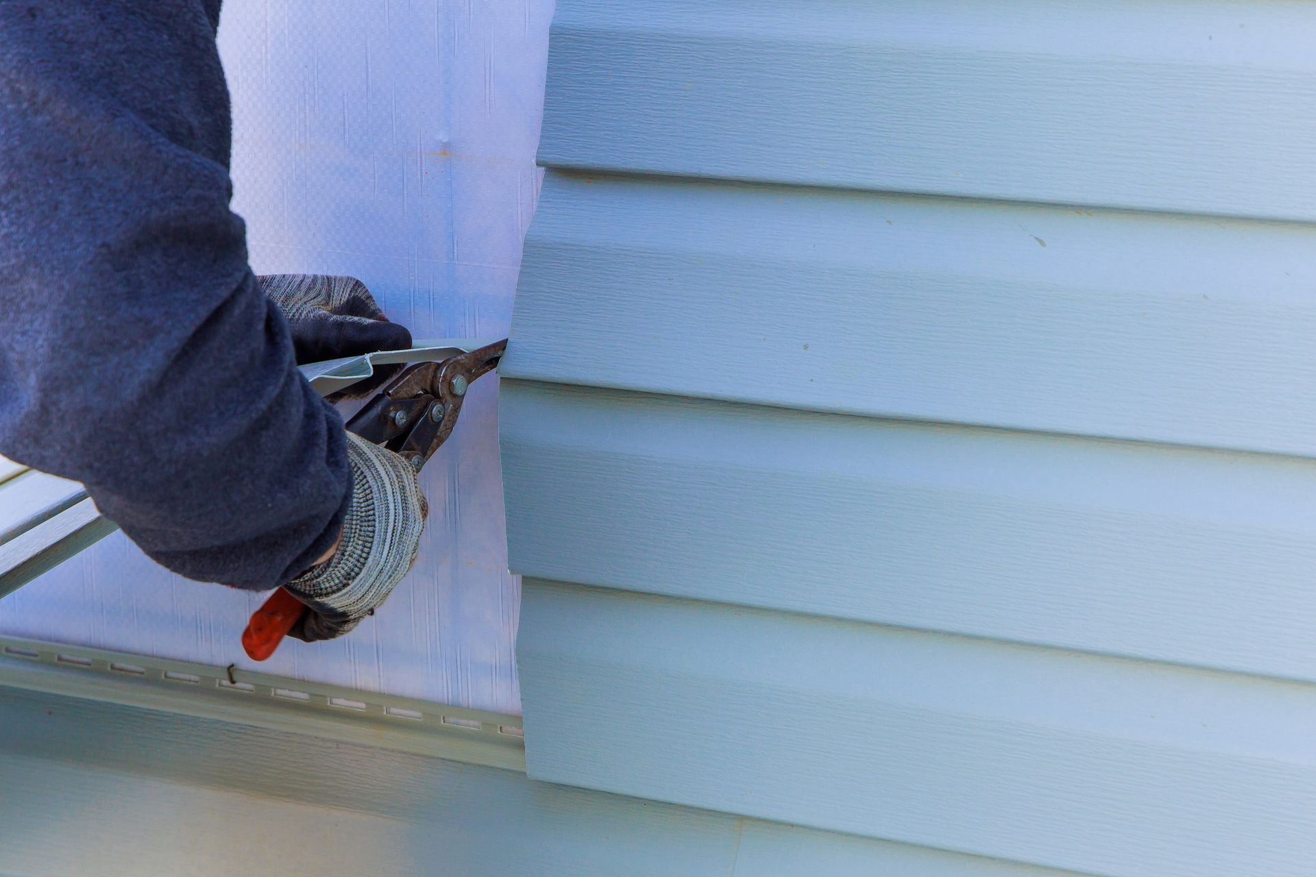 Person cutting vinyl siding with metal shears on a house.