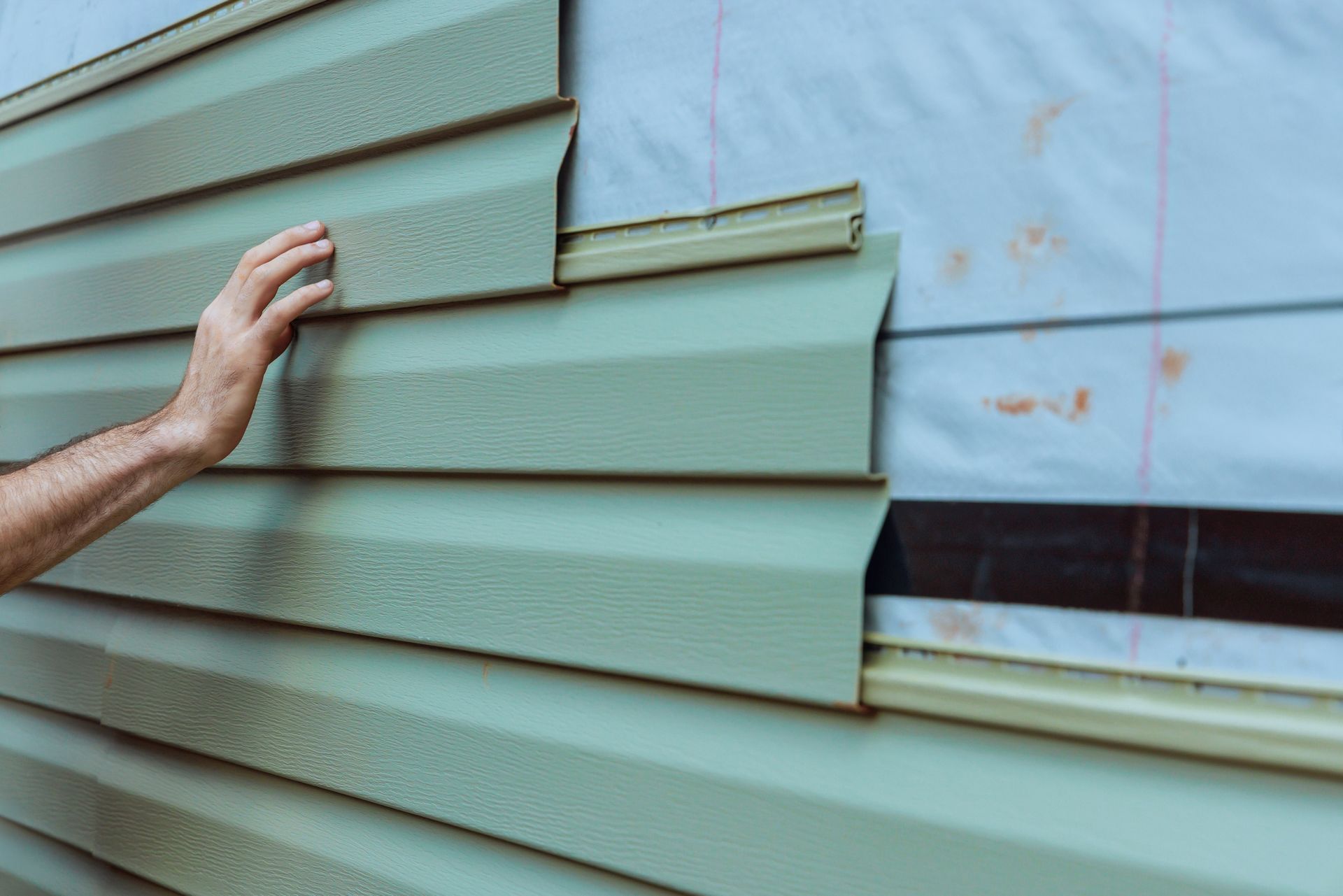 Hand installing light green vinyl siding on a house.