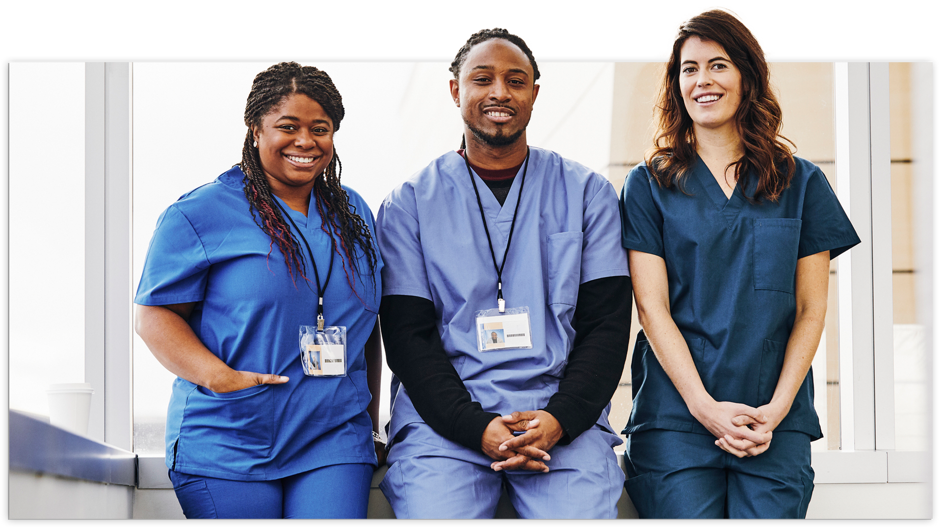 Three healthcare workers smiling in blue scrubs indoors.