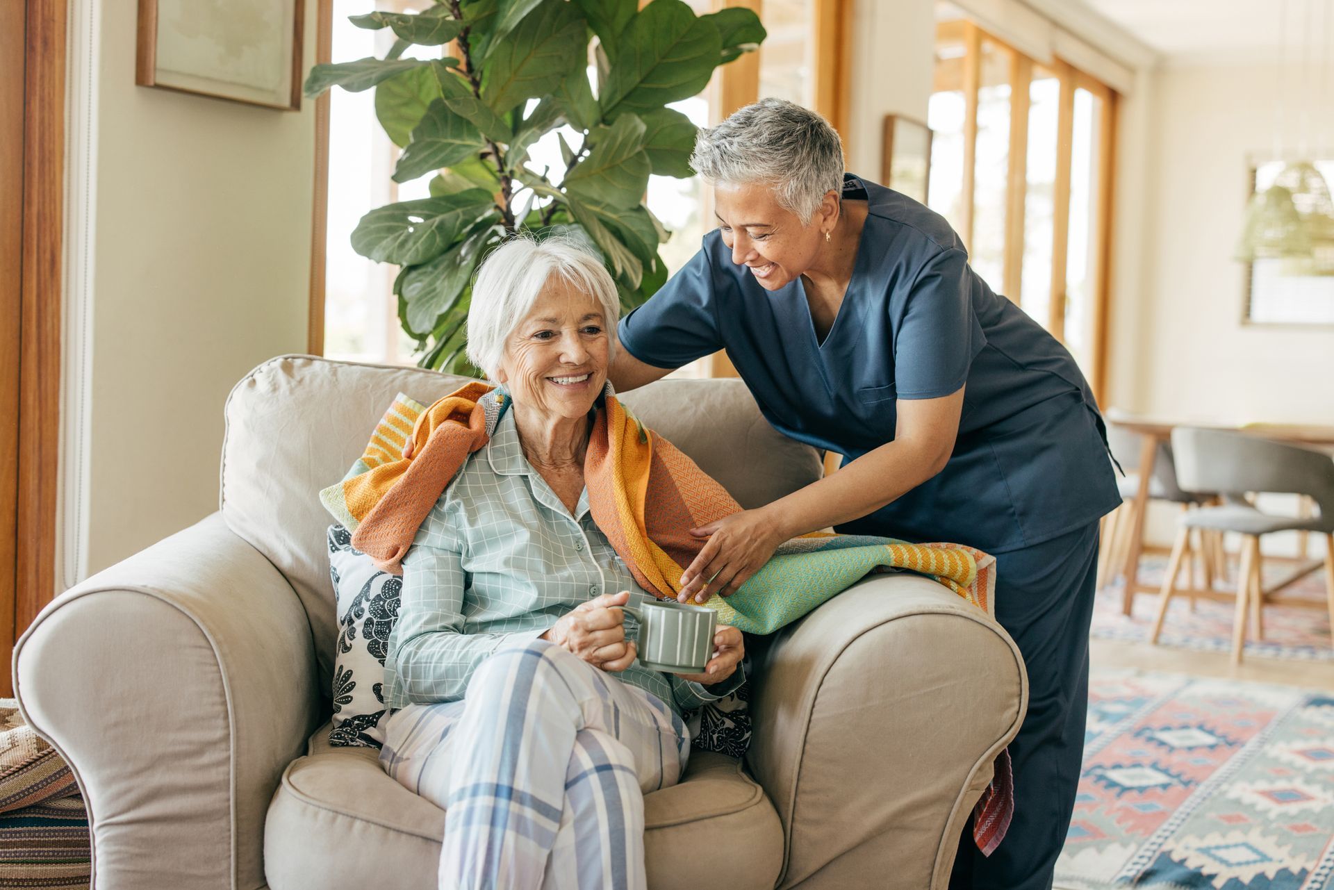 Caregiver assisting a senior woman with a blanket, indoors.