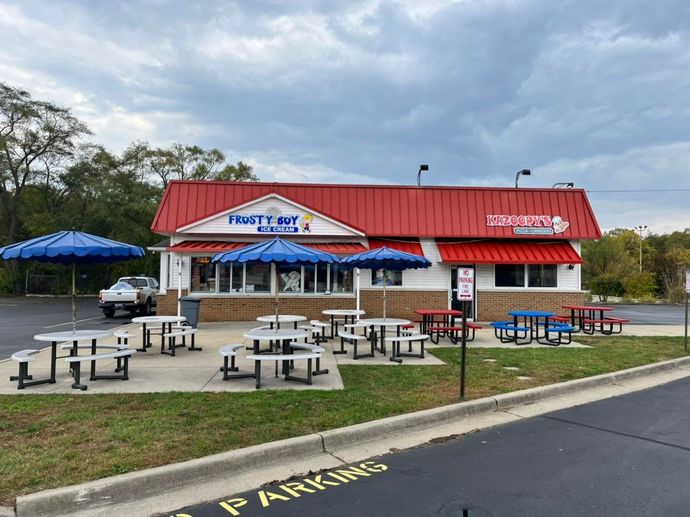 Outdoor picnic area outside a red-roofed fast-food restaurant with blue umbrellas and picnic tables