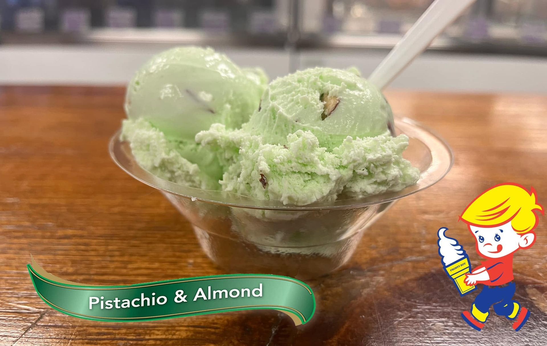 Pistachio almond ice cream in a cup on a table, with a spoon and a flavor label.