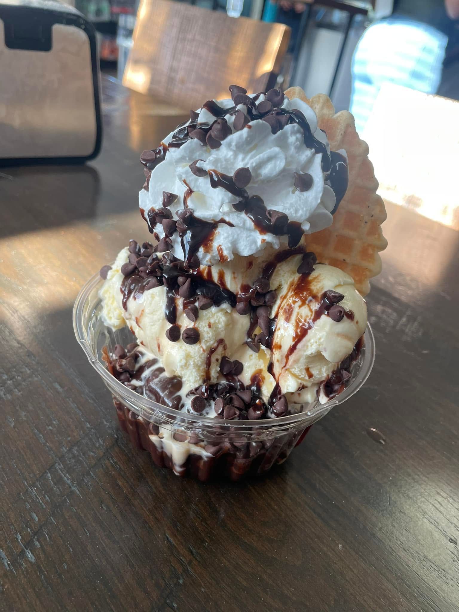 Ice cream sundae with whipped cream and chocolate drizzle in a clear cup on a table