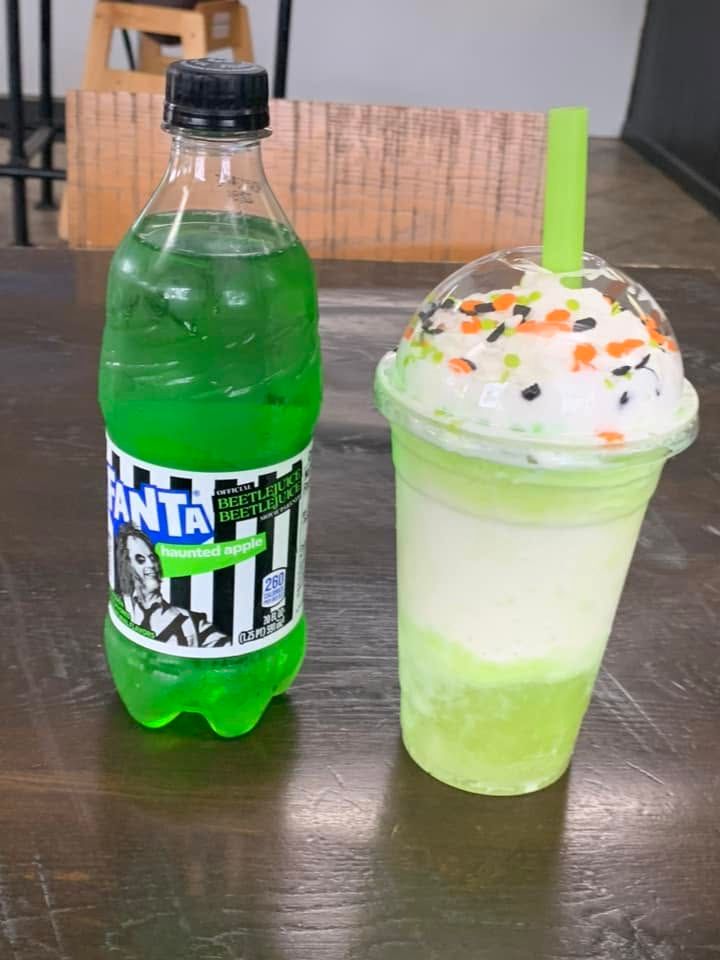 Green soda bottle beside a green frozen drink topped with whipped cream and sprinkles on a table
