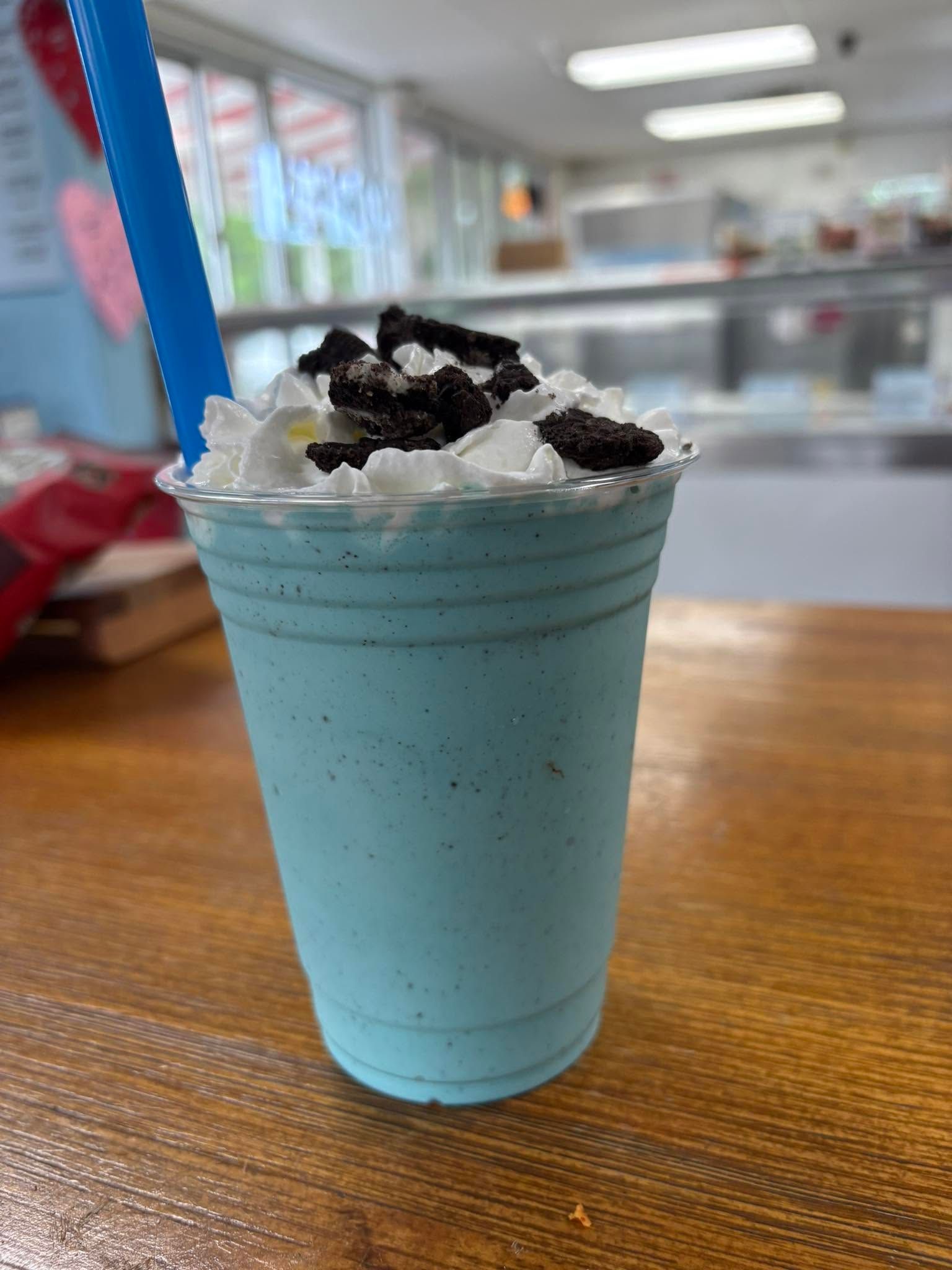 Blue milkshake topped with whipped cream and cookie crumbs on a wooden table