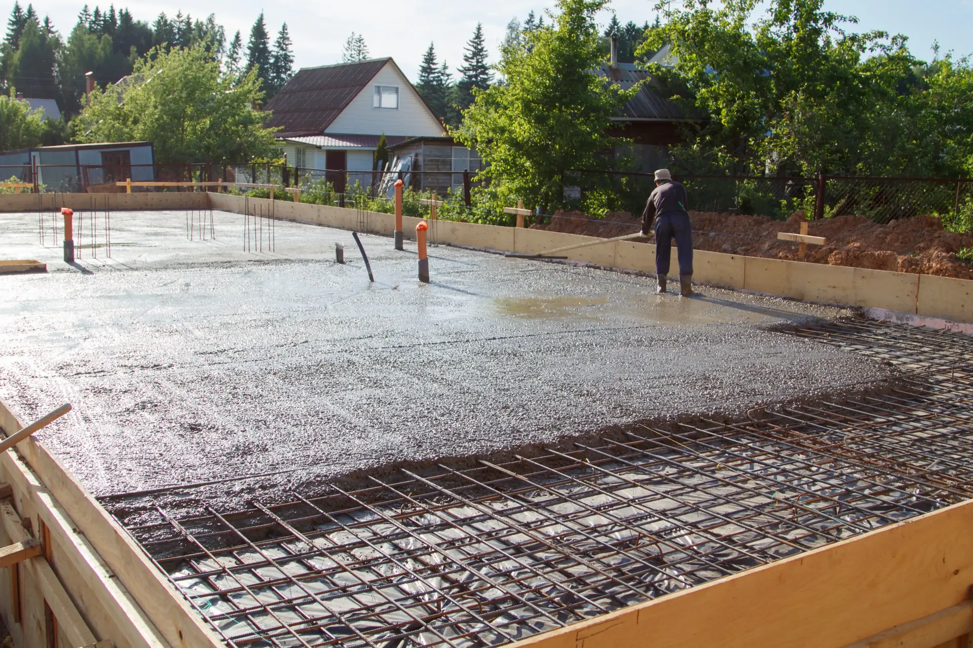 Freshly poured concrete foundation with rebar, wooden formwork, and a person standing, in a residential setting.