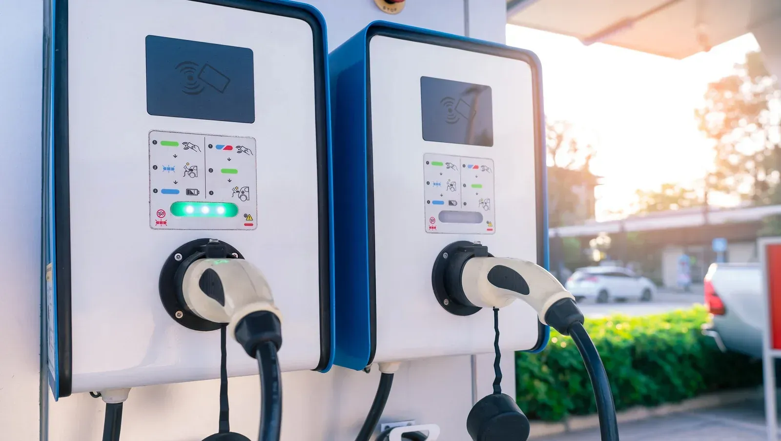 Two electric vehicle charging stations with connected cables and glowing status indicators outdoors.