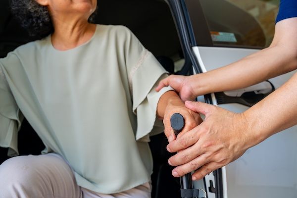 A medical aid helps their patient out of the car