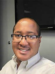 Person wearing glasses smiles in front of a monitor.