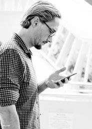 Man looking at phone, wearing glasses and checkered shirt. Side profile, outdoors.