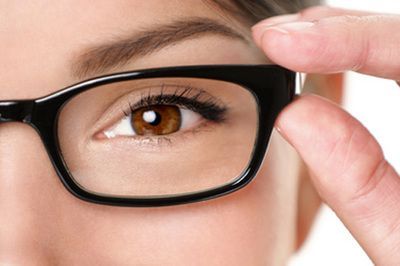 Close-up of a person with brown eyes wearing black-framed glasses, adjusting them with a finger.
