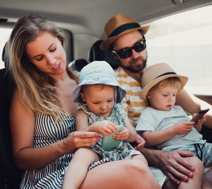 Family in a car. Woman holds baby; man has child on lap. All wear hats.