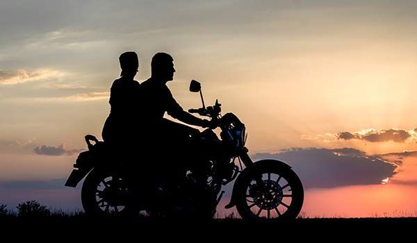 Silhouette of two people riding a motorcycle against a sunset.