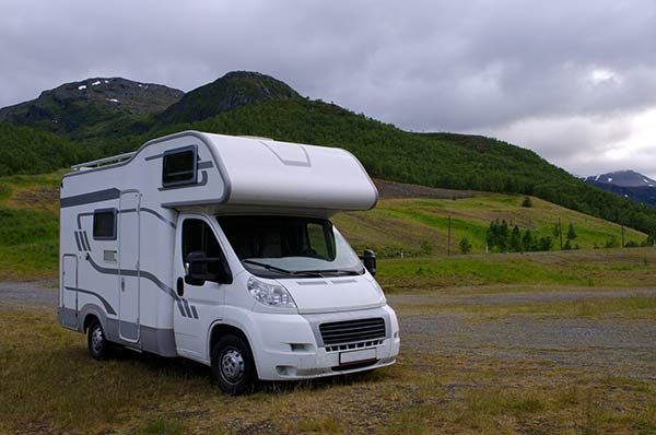 White camper van parked on grass, with mountains in the background under a cloudy sky.