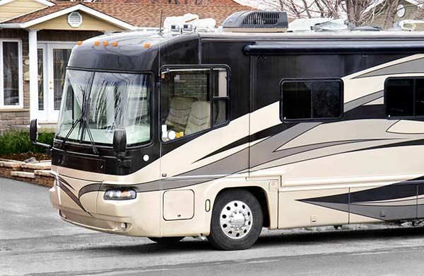 Tan and black RV parked in front of a house.