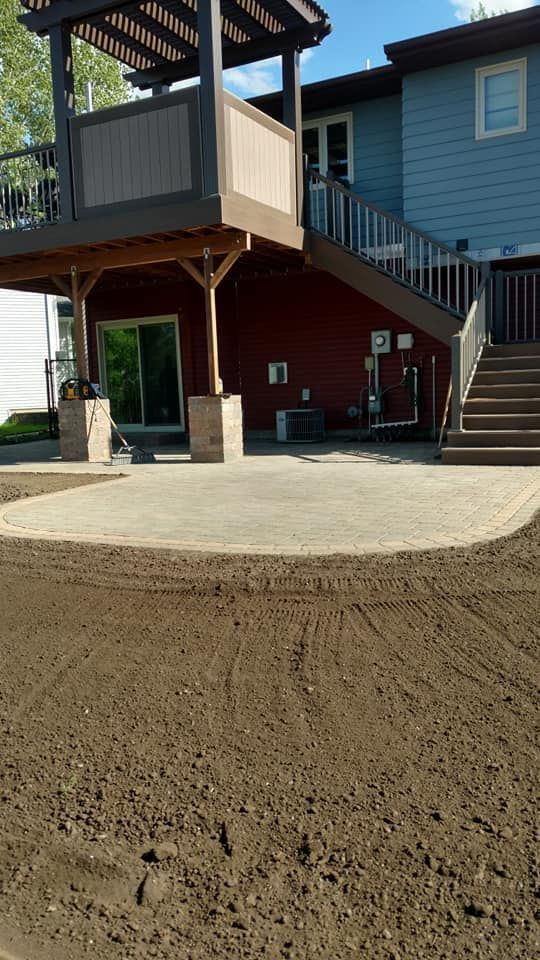 Backyard patio with stairs, raised deck, and blue house exterior at the top of a dirt yard