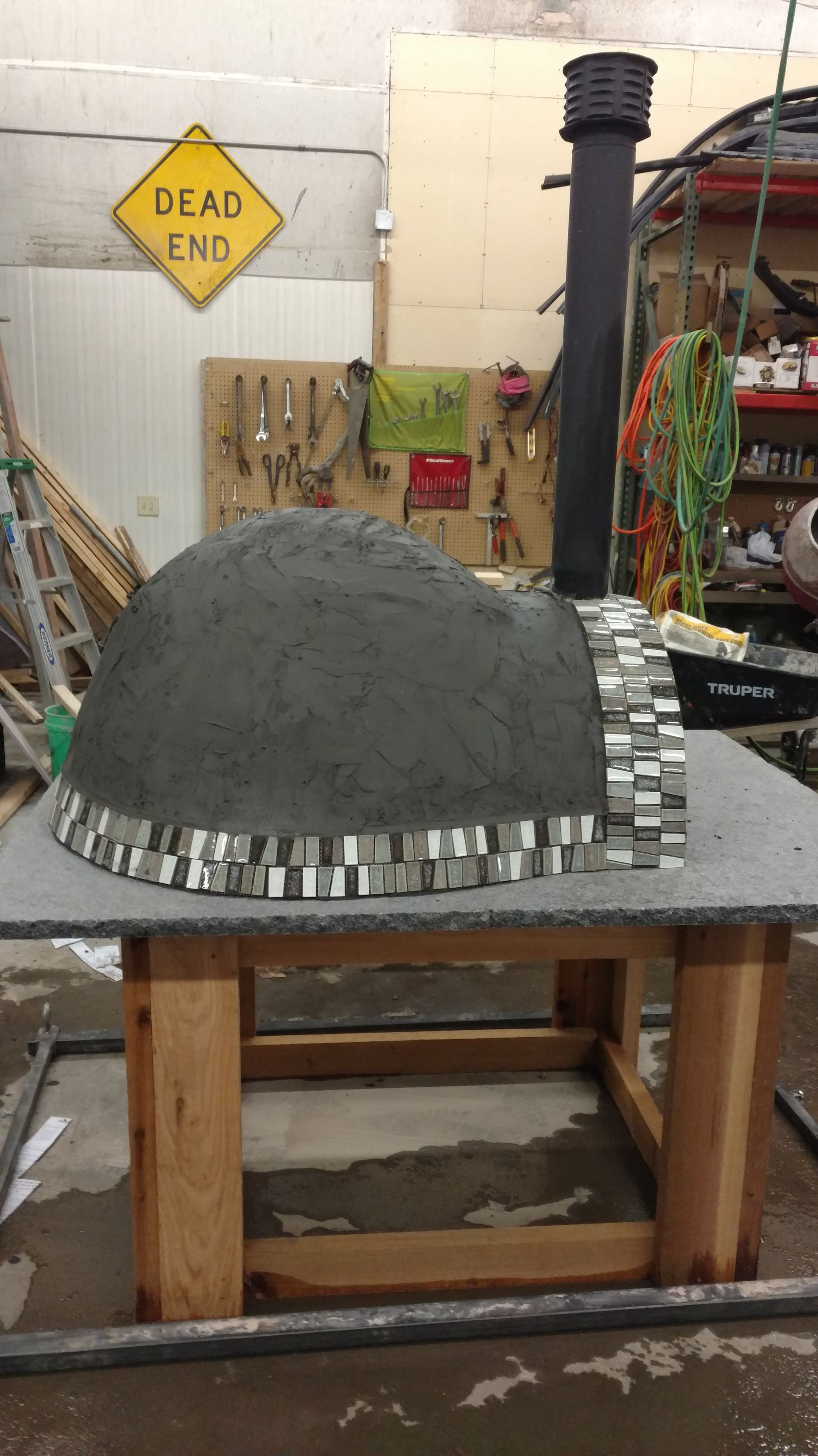 Workbench with a gray dome-shaped model on a striped base in a cluttered workshop.