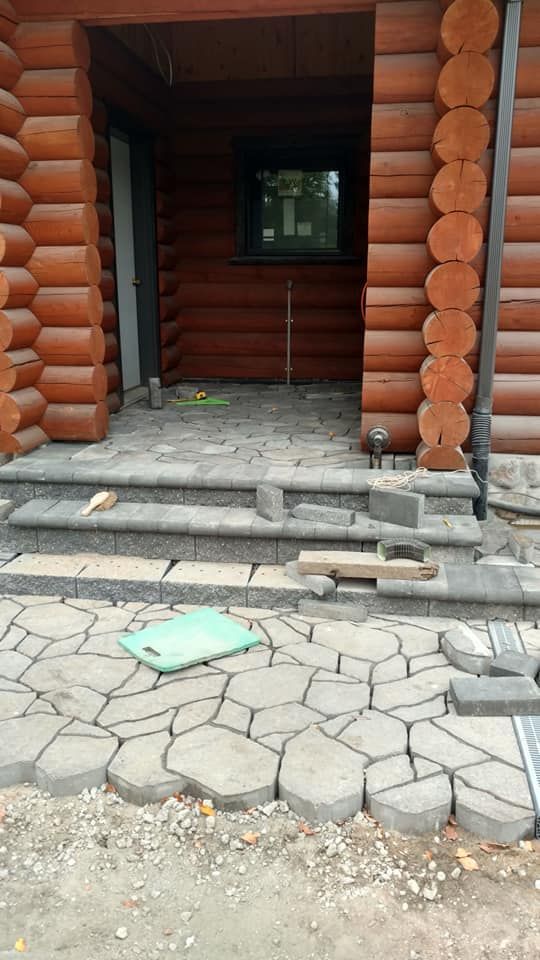 Log cabin entrance with uneven stone steps and cracked paving leading to an open doorway