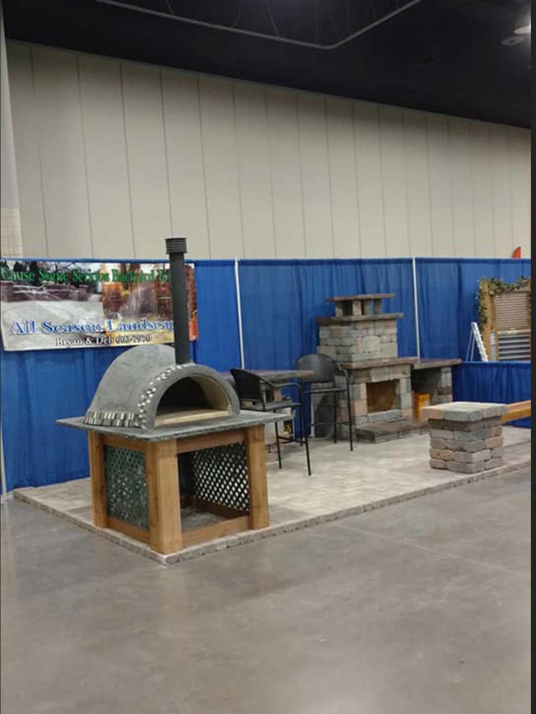Indoor expo booth with several ovens and masonry fireplaces on display, including a domed oven in front.