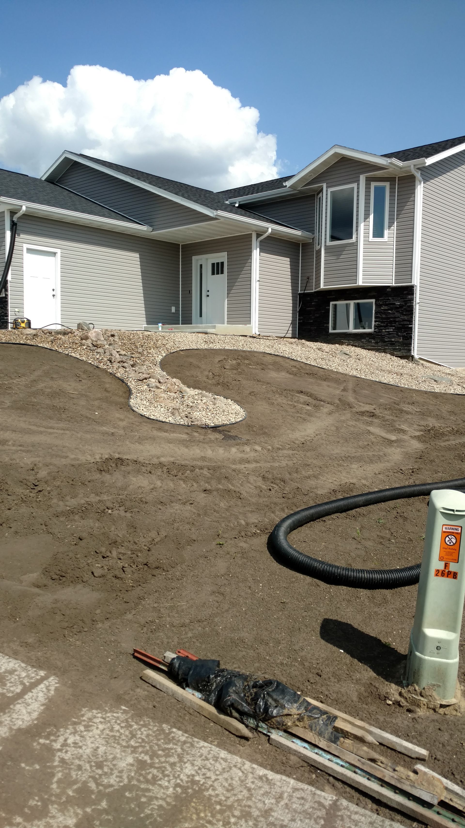 New home exterior with dirt yard, stone walkway, and construction tools in the foreground