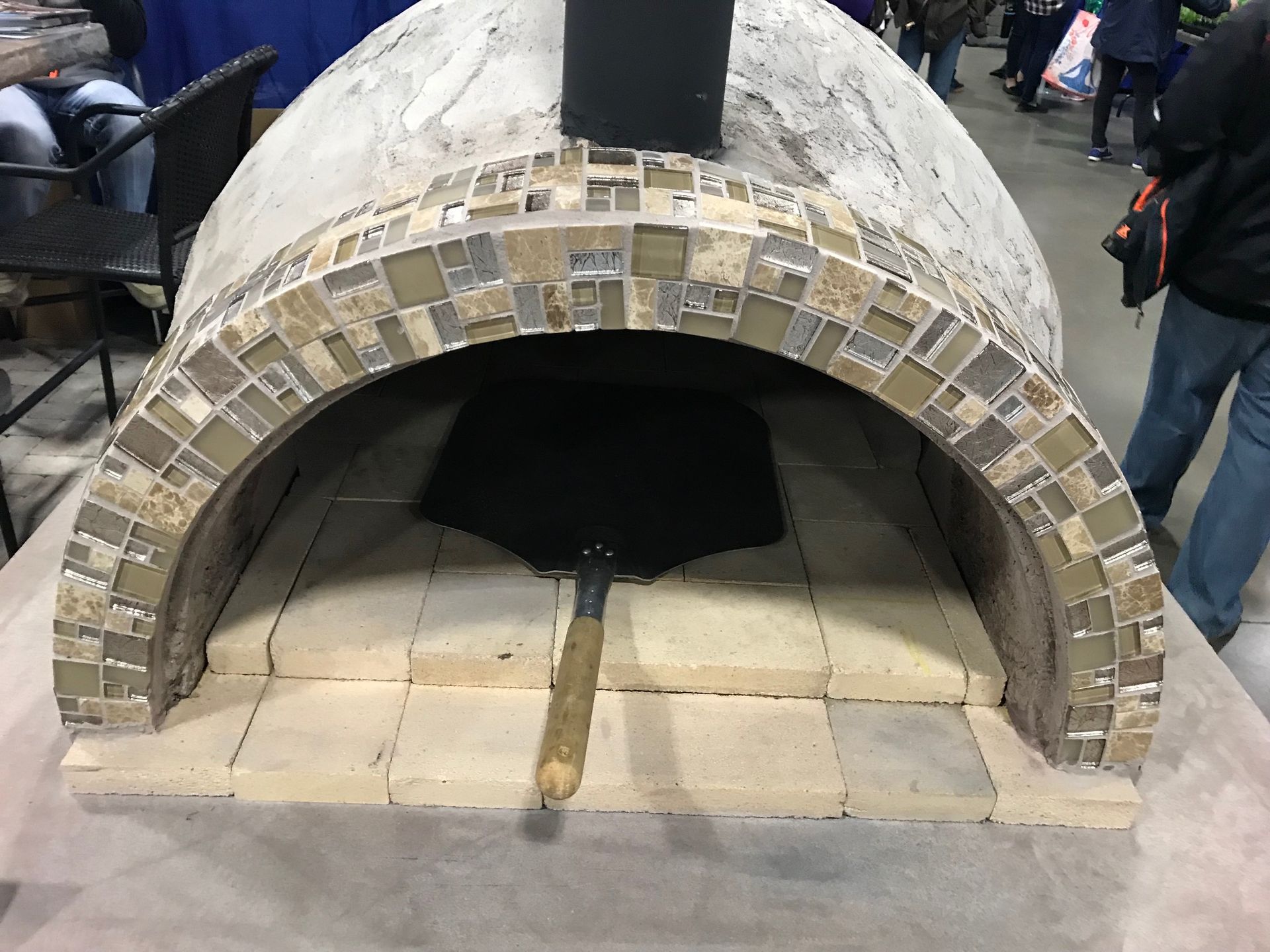 Small brick dome oven with an arched opening and chimney, set on a tiled outdoor floor