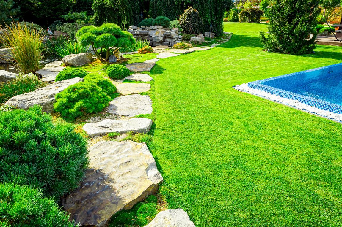 Curved stone path beside a bright green lawn and blue swimming pool in a landscaped garden