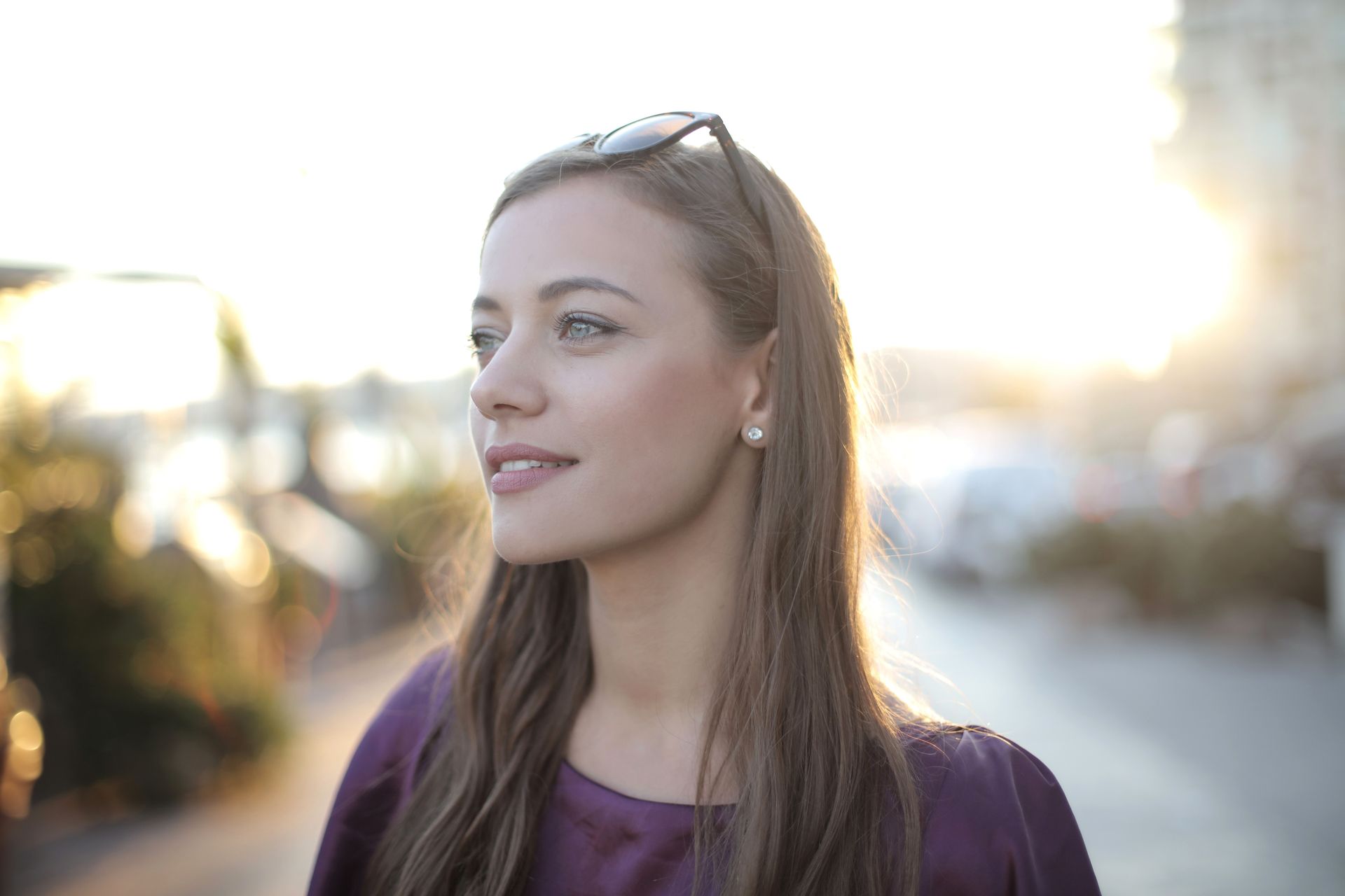 Woman with long hair and sunglasses on her head, smiling outdoors in soft sunlight.