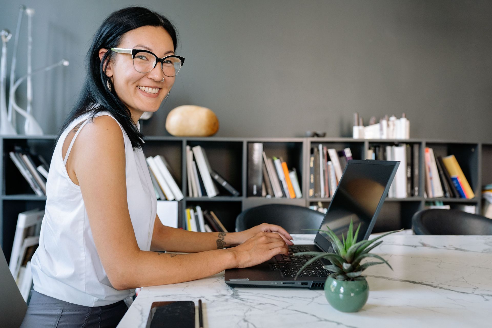 Woman smiling while typing on a laptop at a desk in a modern office