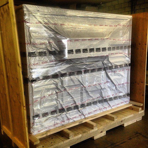 Palletized stack of shrink-wrapped packages in a warehouse, secured on a wooden pallet.