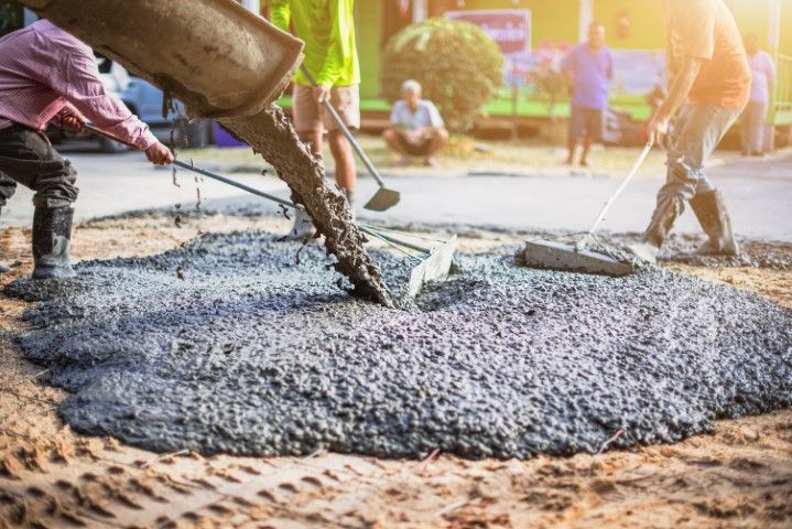 Workers pour wet concrete on a road construction site at sunset.